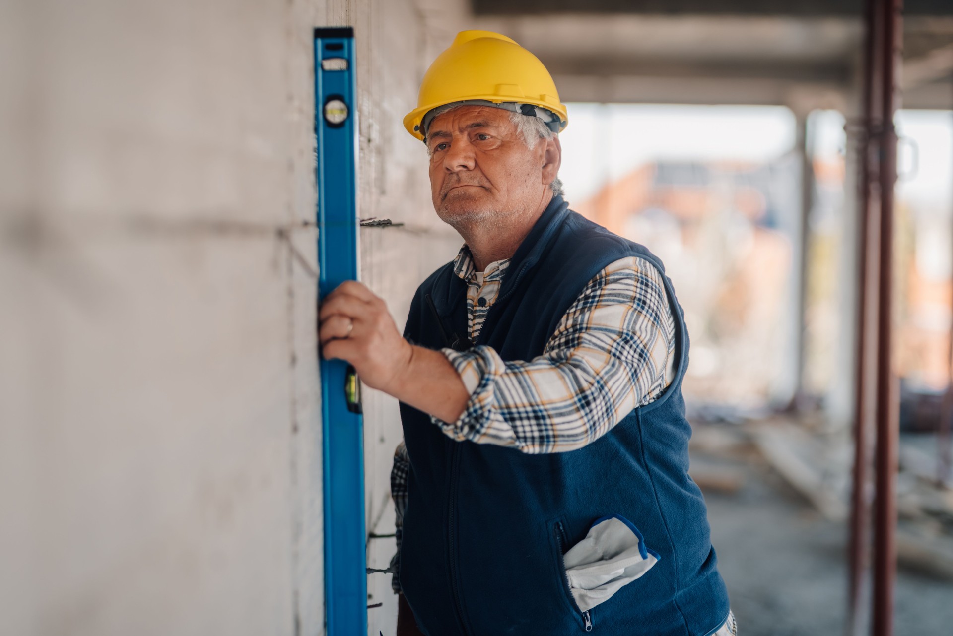 Senior construction worker using spirit level on wall at construction site